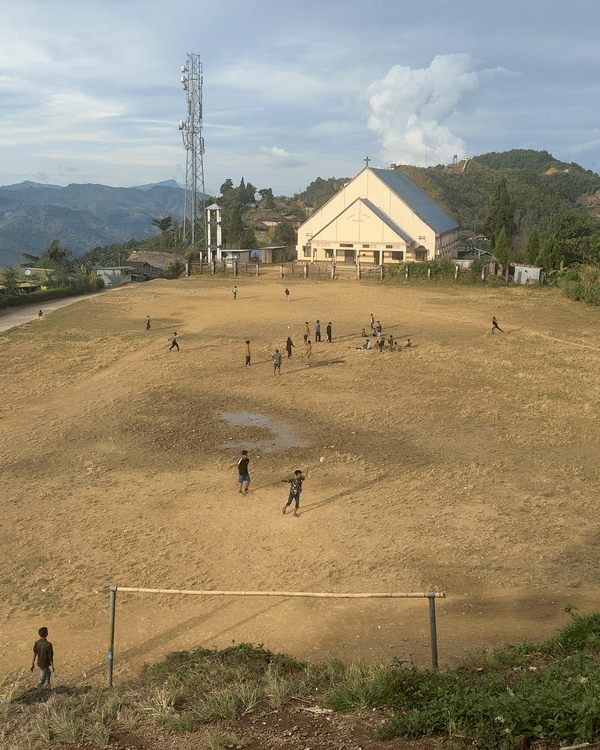 Jeunes jouant sur le terrain de foot au milieu du village Naga devant l'église